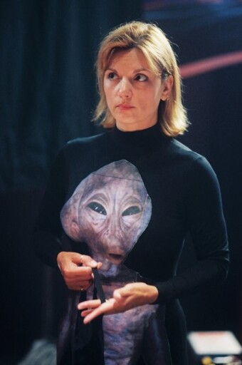 Behind-the-scenes photo of Teryl Rothery wearing an all-black jumpsuit with an Asgard printed on the front, holding a black head/face covering