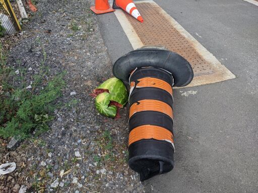A smashed-open watermelon on the ground next to a road pylon