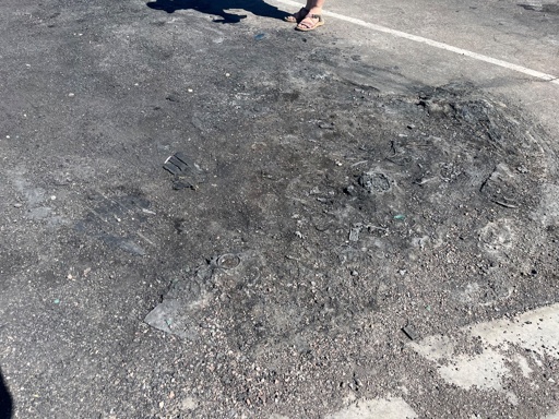 Remains of a burned car melted into an asphalt parking spot